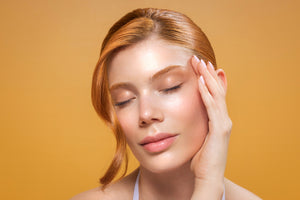 A beautiful woman gently touching her face with closed eyes, surrounded by a bright yellow backdrop, highlighting organic facial moisturizer.