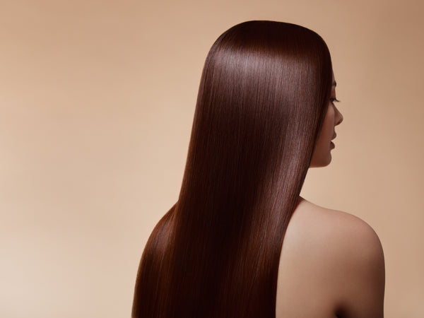Woman with long, straight brown hair, bare shoulders, using our raw hair products